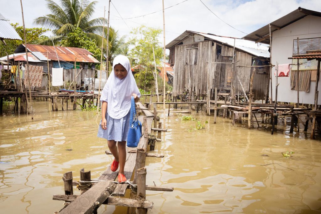 Meisje loopt over brug naar huis door hoog water als gevolg van klimaatverandering