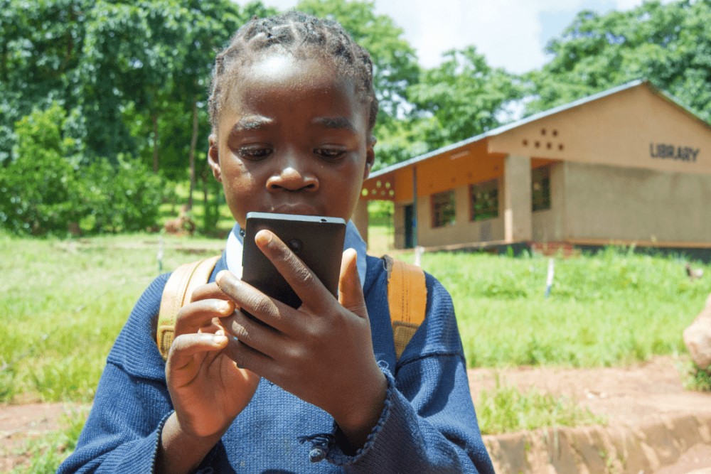 Afrikaans meisje met telfoon die haar helpt om onderwijs te krijgen.