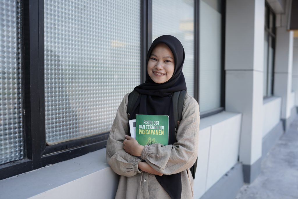 Nuria, een meisje uit Sambas, staat met haar schoolboeken in haar armen en lacht