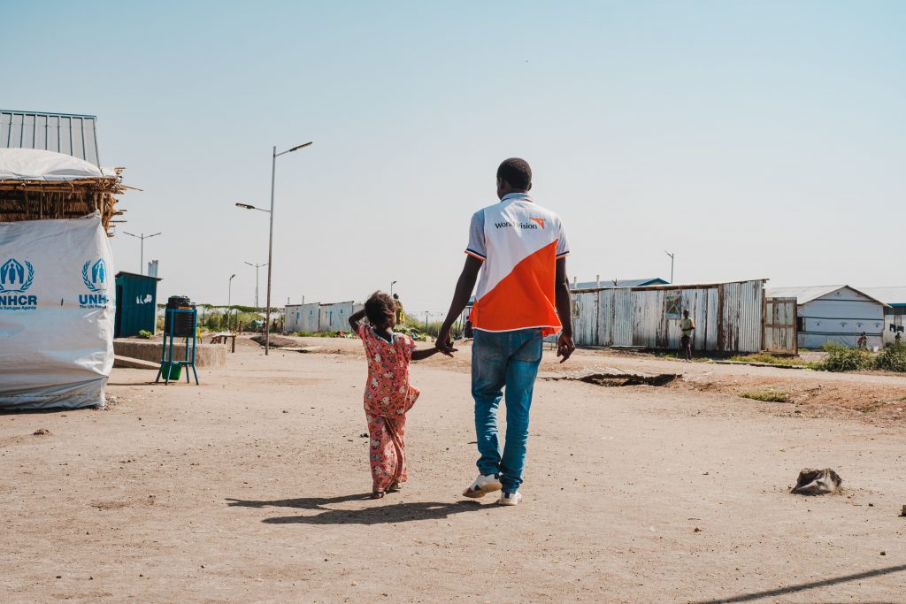 Een World vision hulpverlener neemt een meisje aan de hand en loopt in een dorp.
